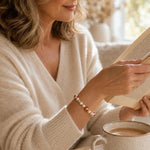 Woman enjoying a quiet morning with coffee and a book while wearing the Meli Swarovski® Crystal Pearl Bracelet featuring cream and rose gold Swarovski® Crystal Pearls.