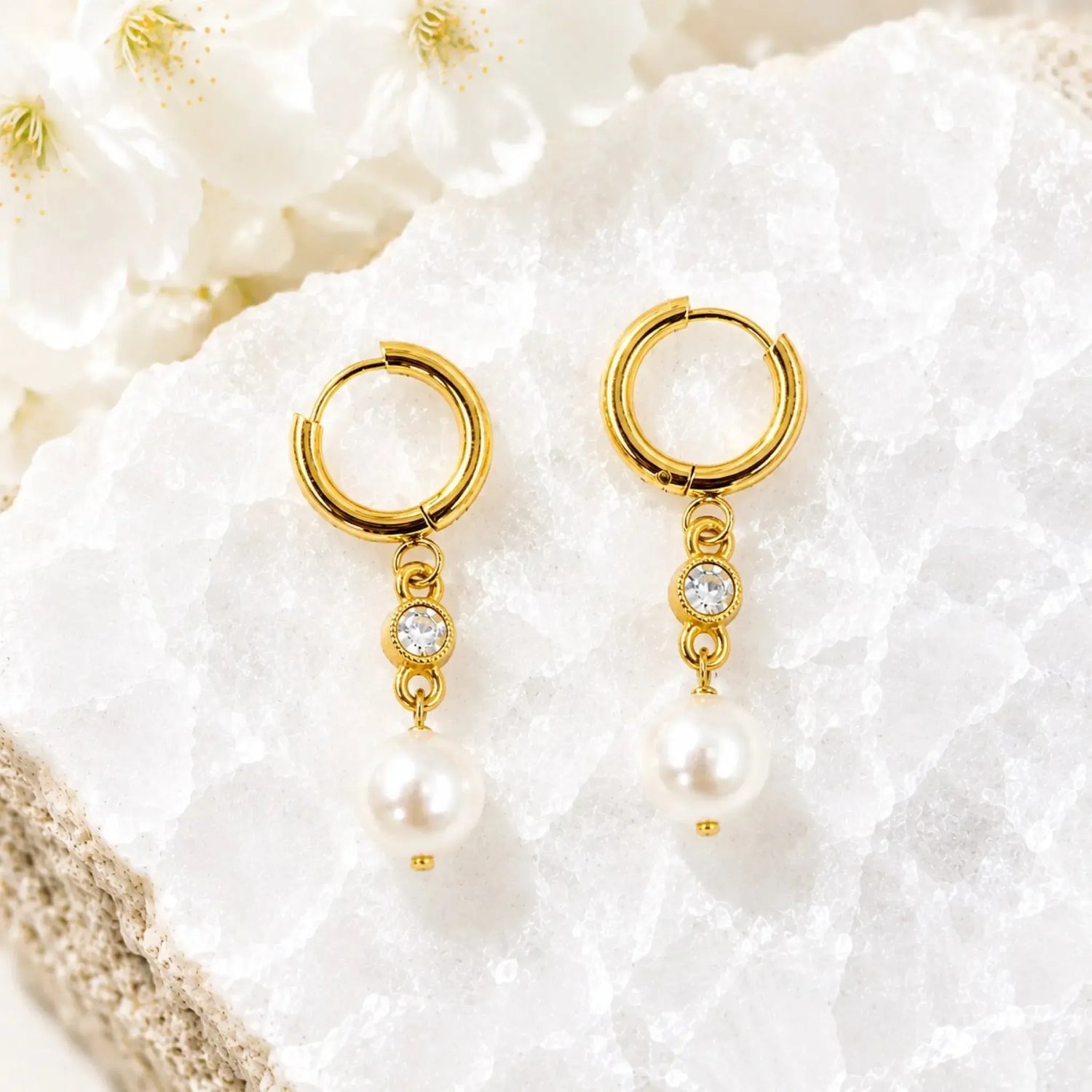 Melia pearl huggie earrings with crystal accents displayed on white quartz, handcrafted gold pearl drop earrings by Carabella by Cheryl.