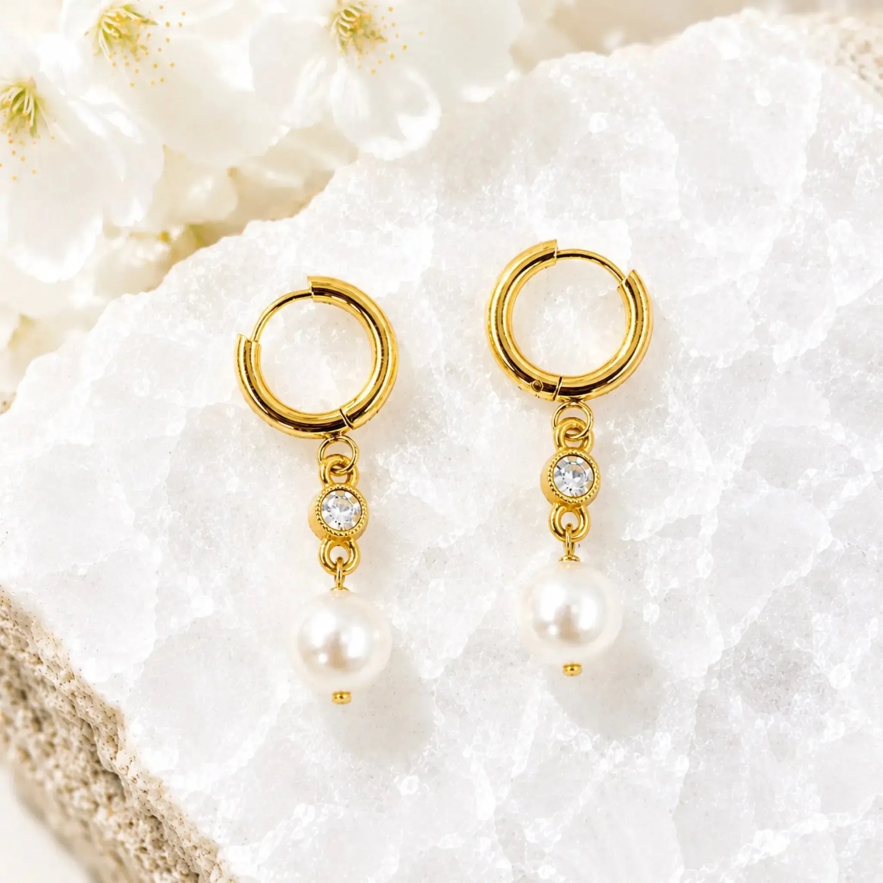 Melia pearl huggie earrings with crystal accents displayed on white quartz, handcrafted gold pearl drop earrings by Carabella by Cheryl.