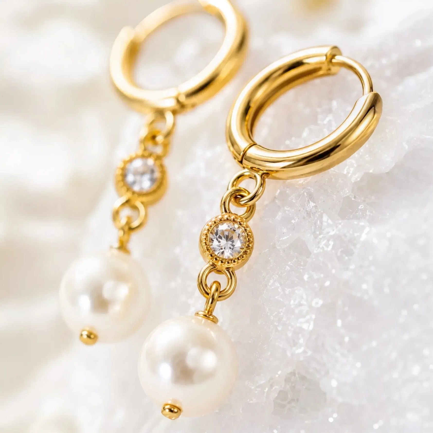 Macro close-up of Melia pearl huggie earrings highlighting the polished gold hoop, crystal setting, pearl attachment, and handcrafted craftsmanship.