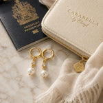 Melia pearl huggie earrings styled with an ivory jewellery pouch, passport, linen scarf, and sunglasses for elegant luxury travel.