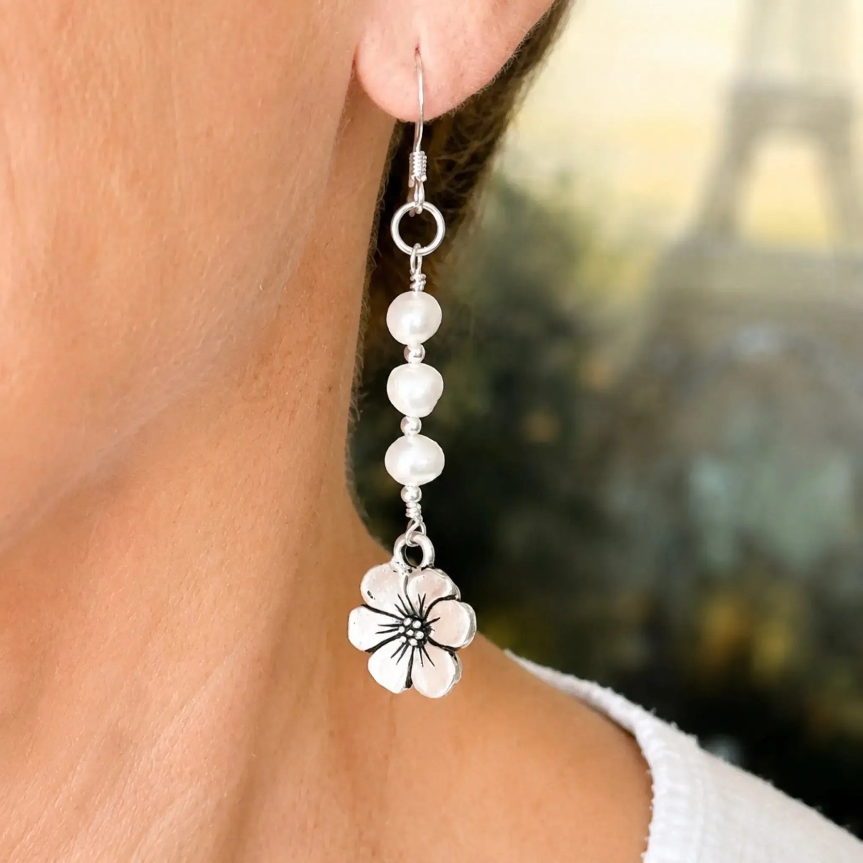 Close-up of Mia Freshwater Pearl Earrings worn on the ear, highlighting genuine freshwater pearls, sterling silver components, and detailed apple blossom charm.