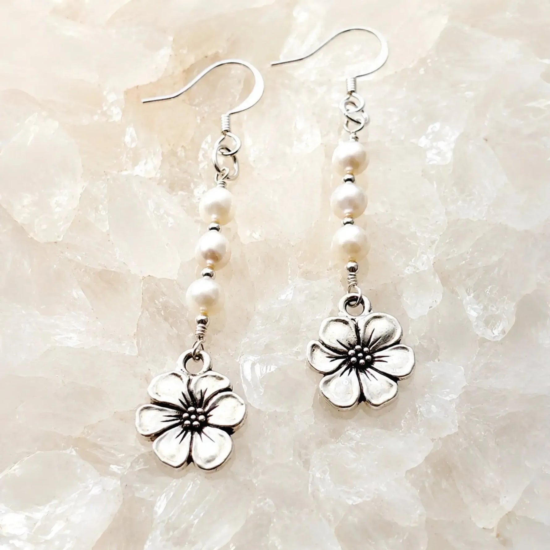 Mia Freshwater Pearl Earrings resting on luminous white quartz crystal, featuring genuine freshwater pearls, sterling silver ear wires, and detailed pewter apple blossom charms.