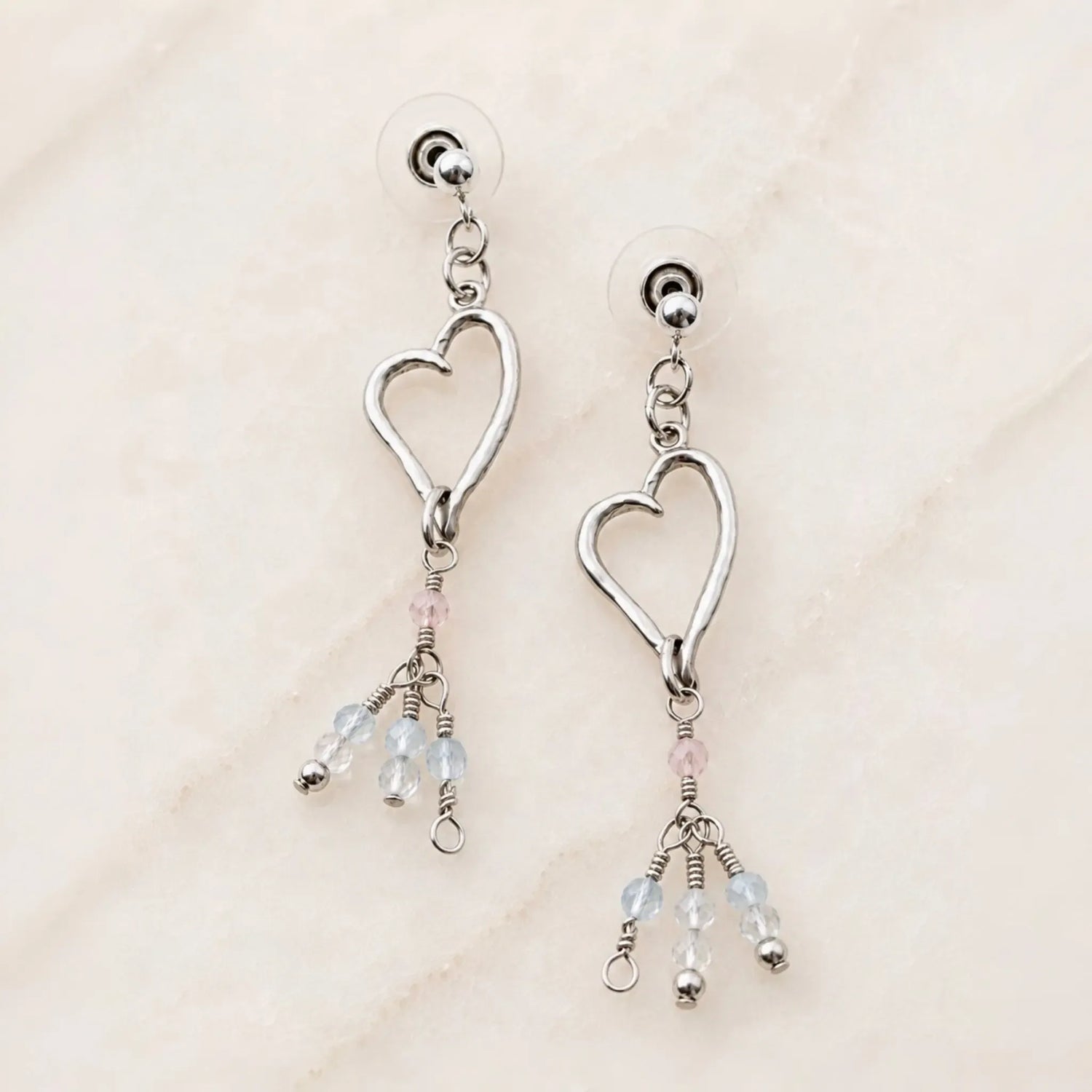 Angled view of handcrafted sterling silver Morganite Heart Earrings with blush morganite and soft blue gemstone tassels.