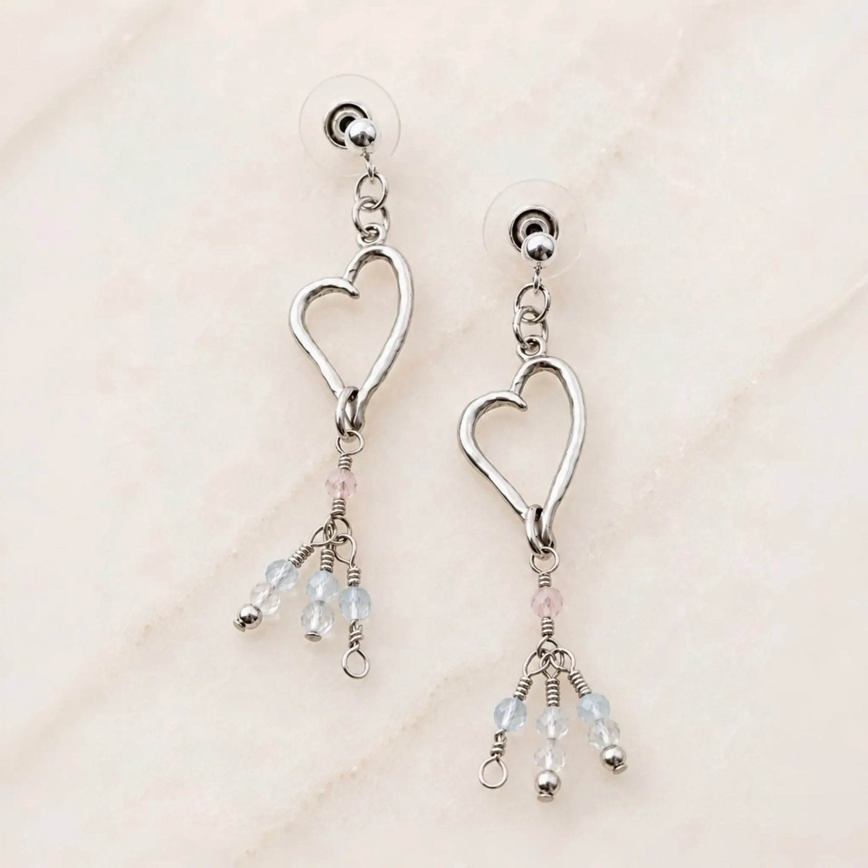 Angled view of handcrafted sterling silver Morganite Heart Earrings with blush morganite and soft blue gemstone tassels.