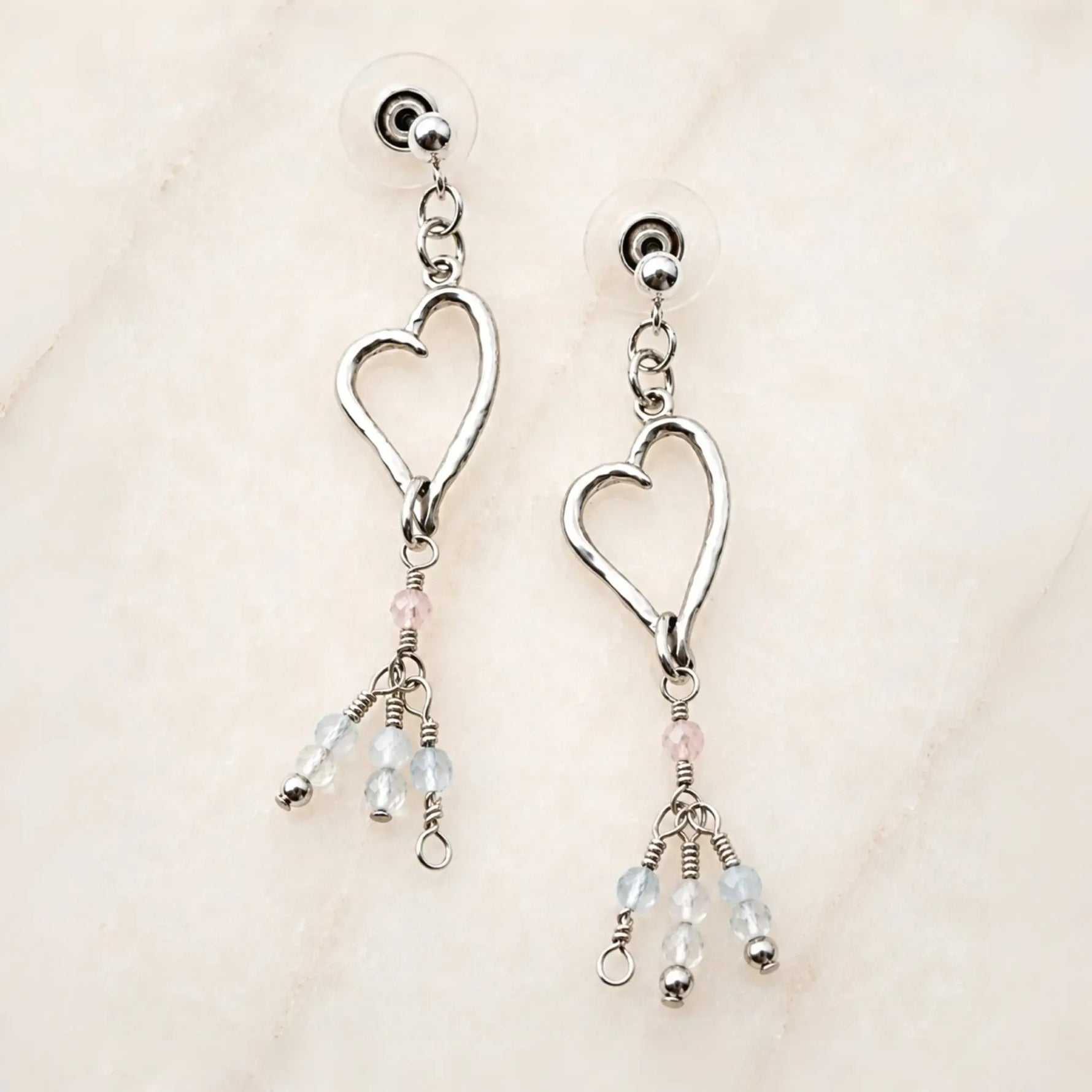 Morganite Heart Earrings handcrafted in sterling silver with blush morganite and soft blue gemstone accents on a white quartz background.