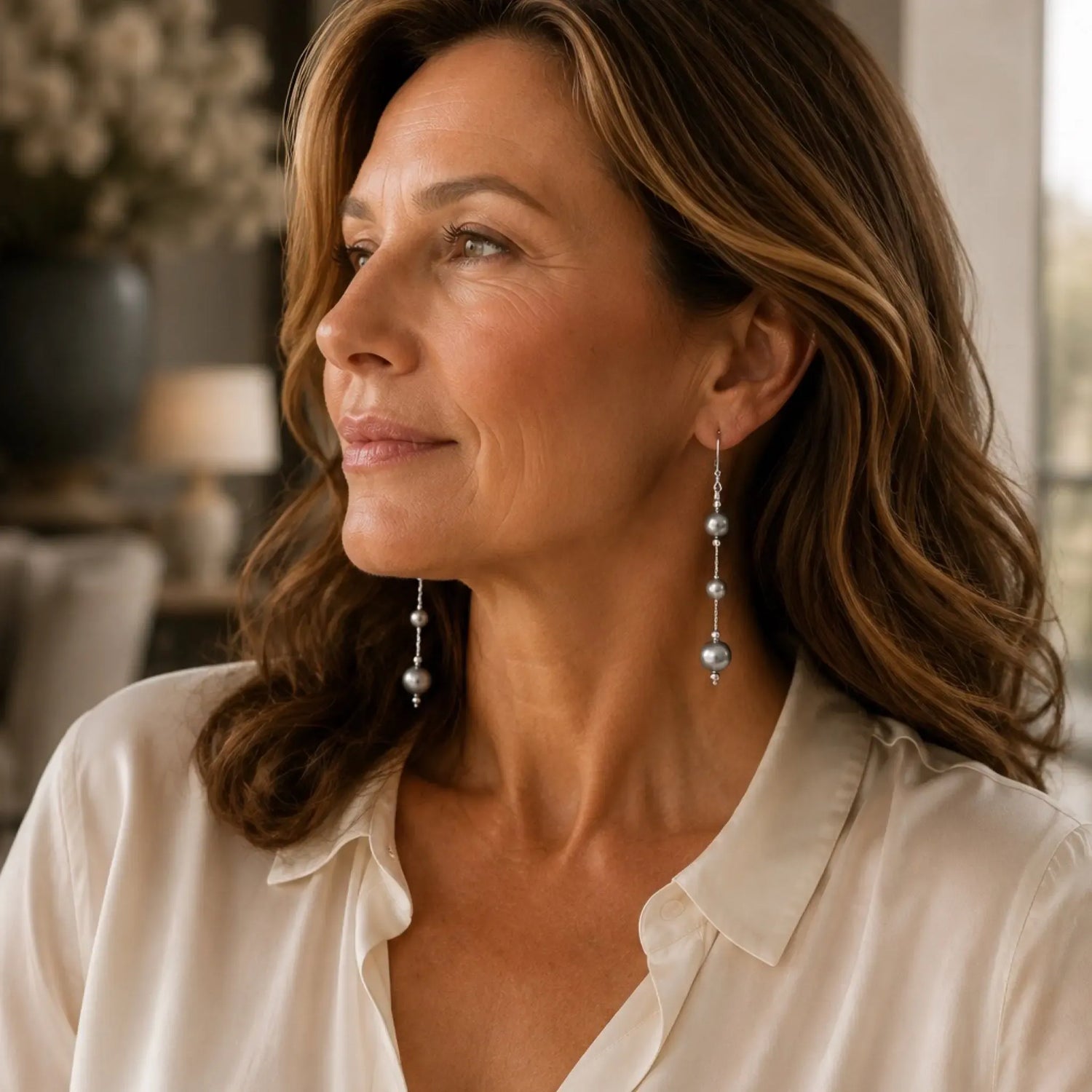 Woman wearing Natasha Swarovski® Crystal Pearl Earrings in an elegant luxury interior with soft natural window light and an ivory silk blouse.