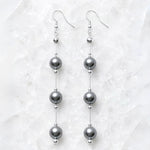 Natasha Swarovski® Crystal Pearl Earrings displayed on Carabella's signature white quartz background, featuring luminous dark grey Swarovski® Crystal Pearls with polished sterling silver accents.