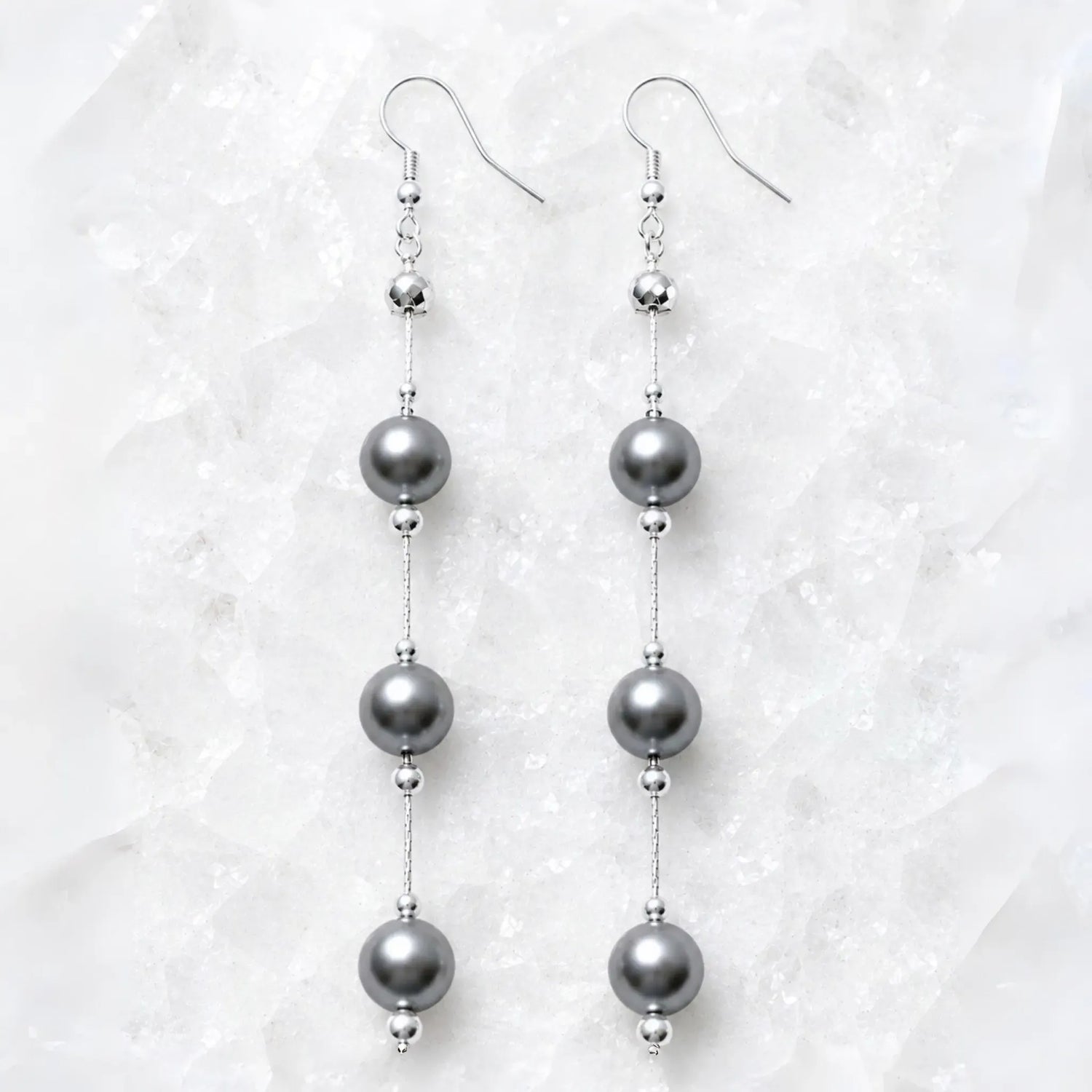 Natasha Swarovski® Crystal Pearl Earrings displayed on Carabella's signature white quartz background, featuring luminous dark grey Swarovski® Crystal Pearls with polished sterling silver accents.