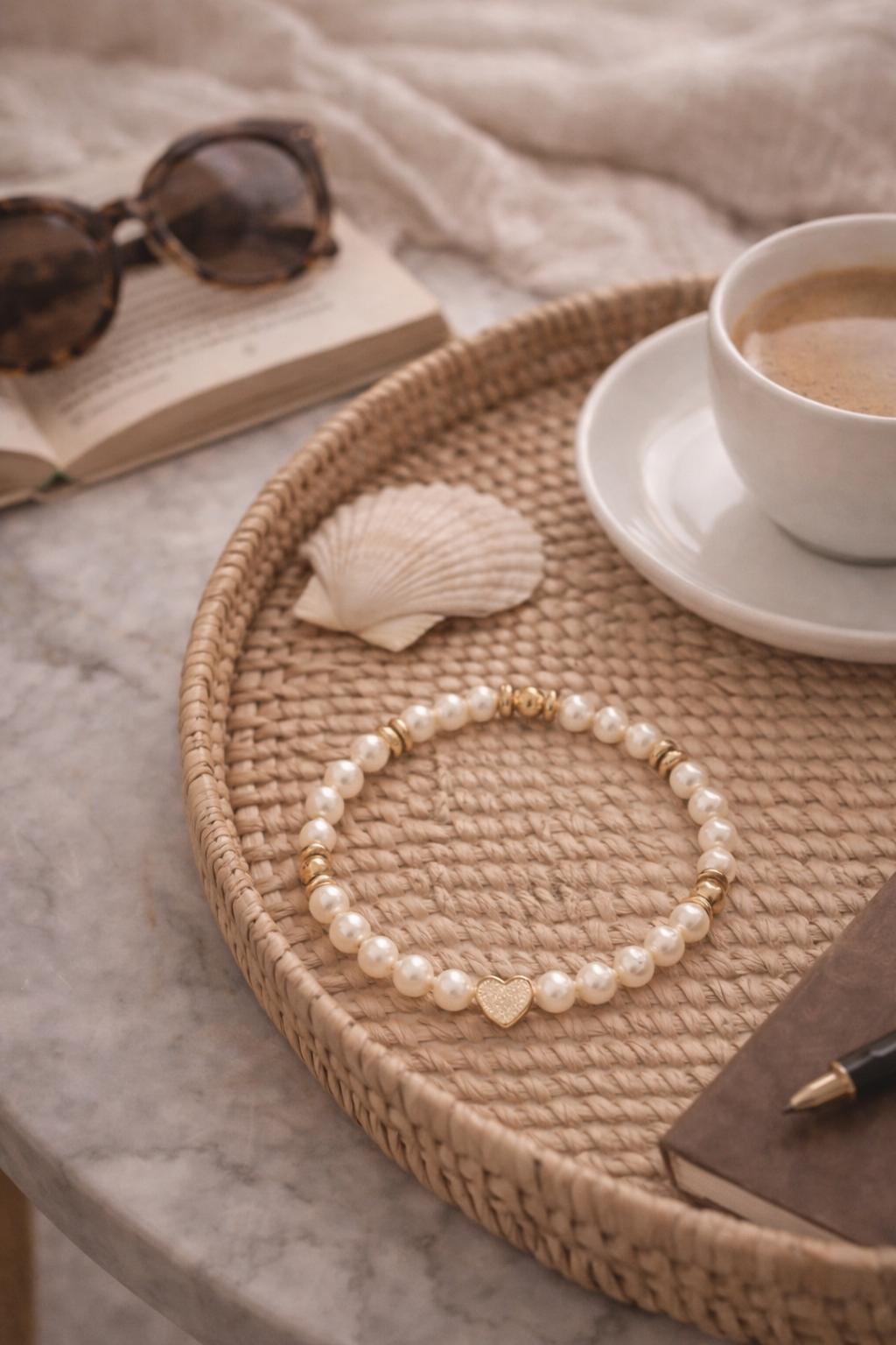 Pandora pearl and gold heart bracelet styled on a woven tray with shell, book, and coffee for a relaxed weekend aesthetic