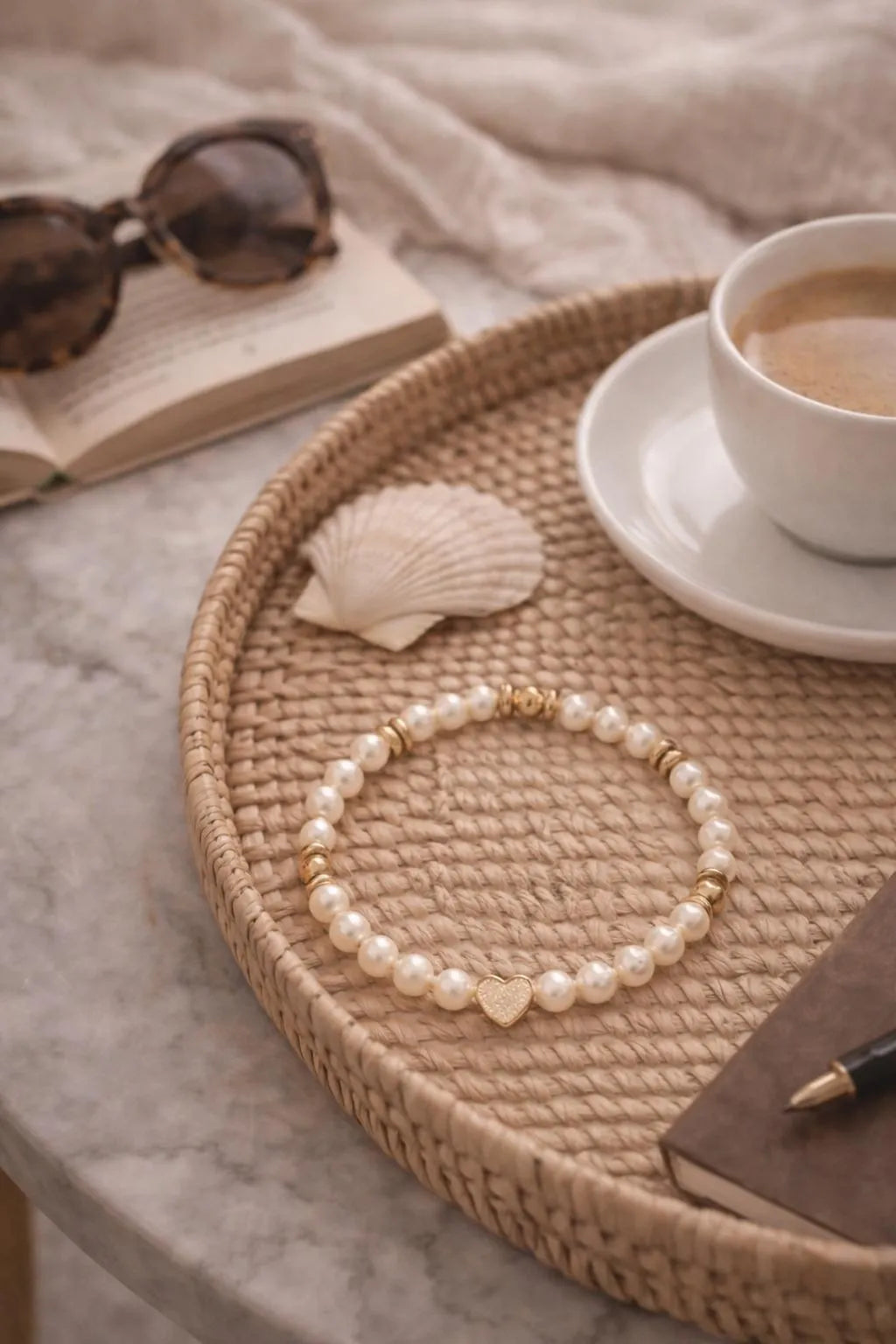 Pandora pearl and gold heart bracelet styled on a woven tray with shell, book, and coffee for a relaxed weekend aesthetic