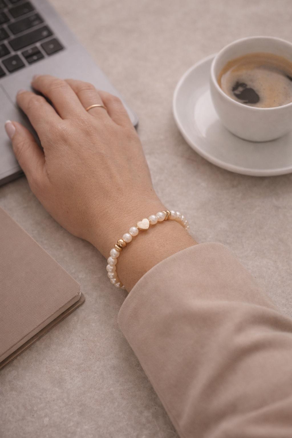 Pandora pearl and gold heart bracelet worn on the wrist in a polished professional setting with laptop and coffee