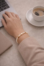 Pandora pearl and gold heart bracelet worn on the wrist in a polished professional setting with laptop and coffee
