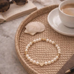 Pandora Swarovski® Crystal Pearl and gold heart bracelet styled on a woven tray with coffee, book, and neutral accessories, highlighting elegant everyday luxury and refined versatility.