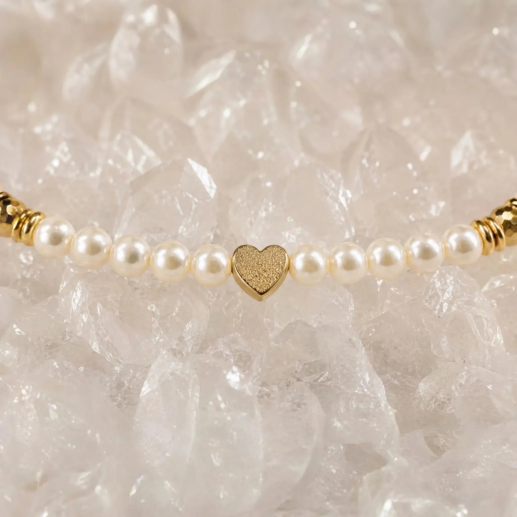 Macro detail of the Pandora Swarovski® Crystal Pearl Bracelet showcasing the textured gold heart centerpiece framed by cream Swarovski® Crystal Pearls atop luminous white quartz crystal.