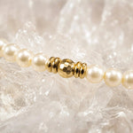 Close-up macro view of the Pandora Swarovski® Crystal Pearl and gold bracelet showcasing faceted gold hematite bead, polished spacer details, and cream Swarovski® Crystal Pearls on white quartz crystal.