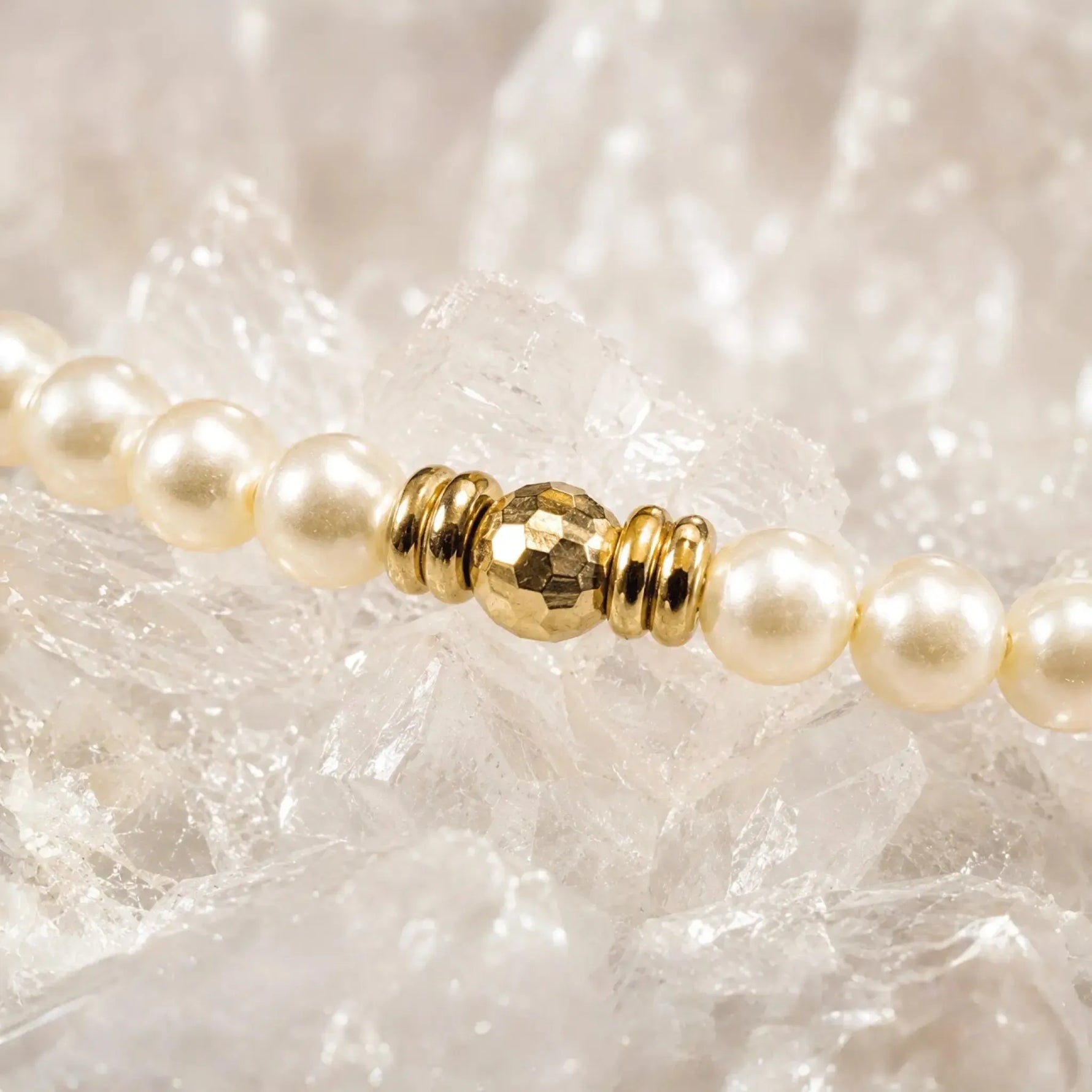 Close-up macro view of the Pandora Swarovski® Crystal Pearl and gold bracelet showcasing faceted gold hematite bead, polished spacer details, and cream Swarovski® Crystal Pearls on white quartz crystal.