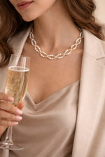 Woman wearing freshwater pearl necklace with gold accents holding a champagne glass, elegant evening jewelry styled with neutral tones.