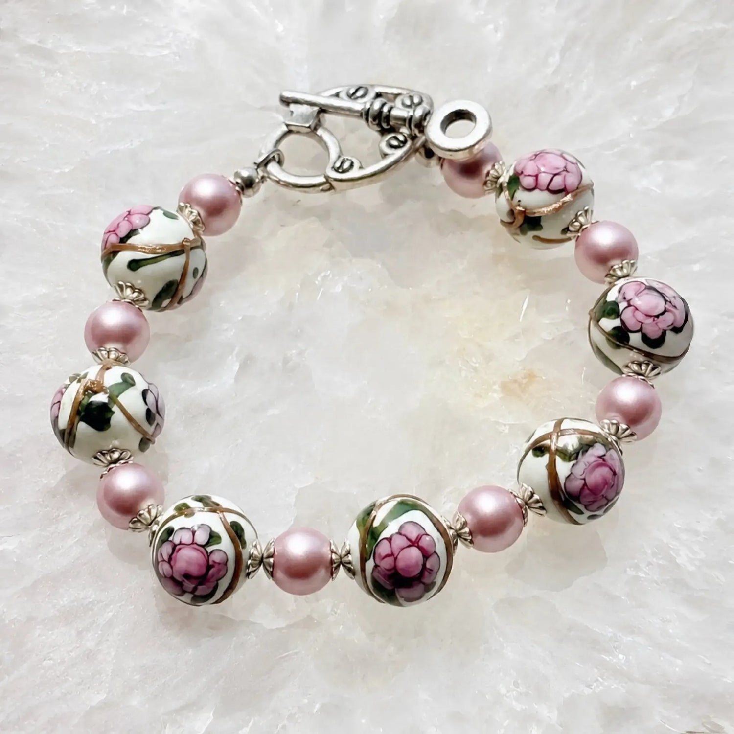 Peony Murano glass bracelet with hand-painted floral beads, pink Swarovski® Crystal Pearls and sterling silver accents on a white quartz surface.