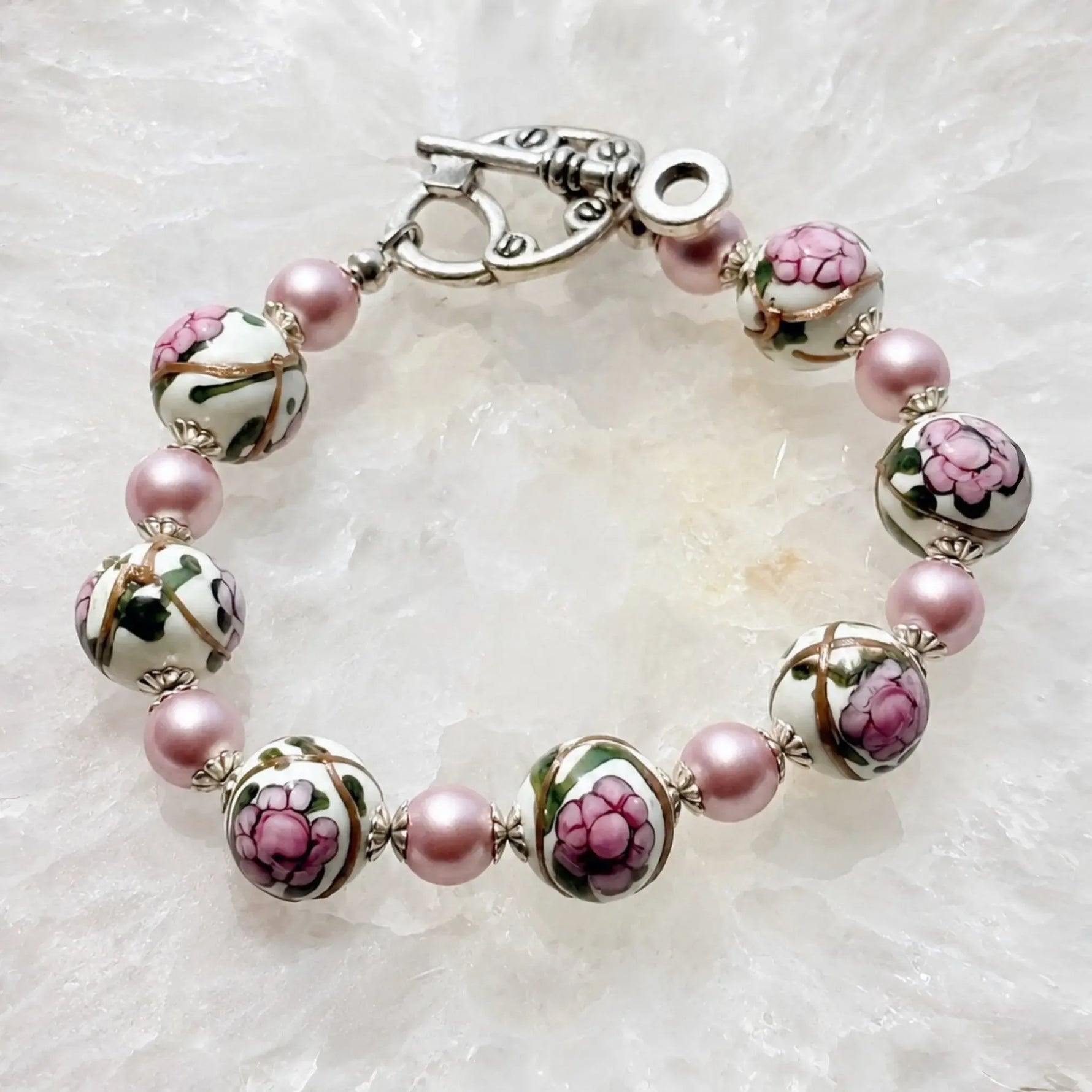 Peony Murano glass bracelet with hand-painted floral beads, pink Swarovski® Crystal Pearls and sterling silver accents on a white quartz surface.