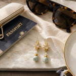 Quianna handcrafted lucky jade drop earrings styled with a passport, sunglasses, and luxury travel accessories on the Carabella signature white quartz background.