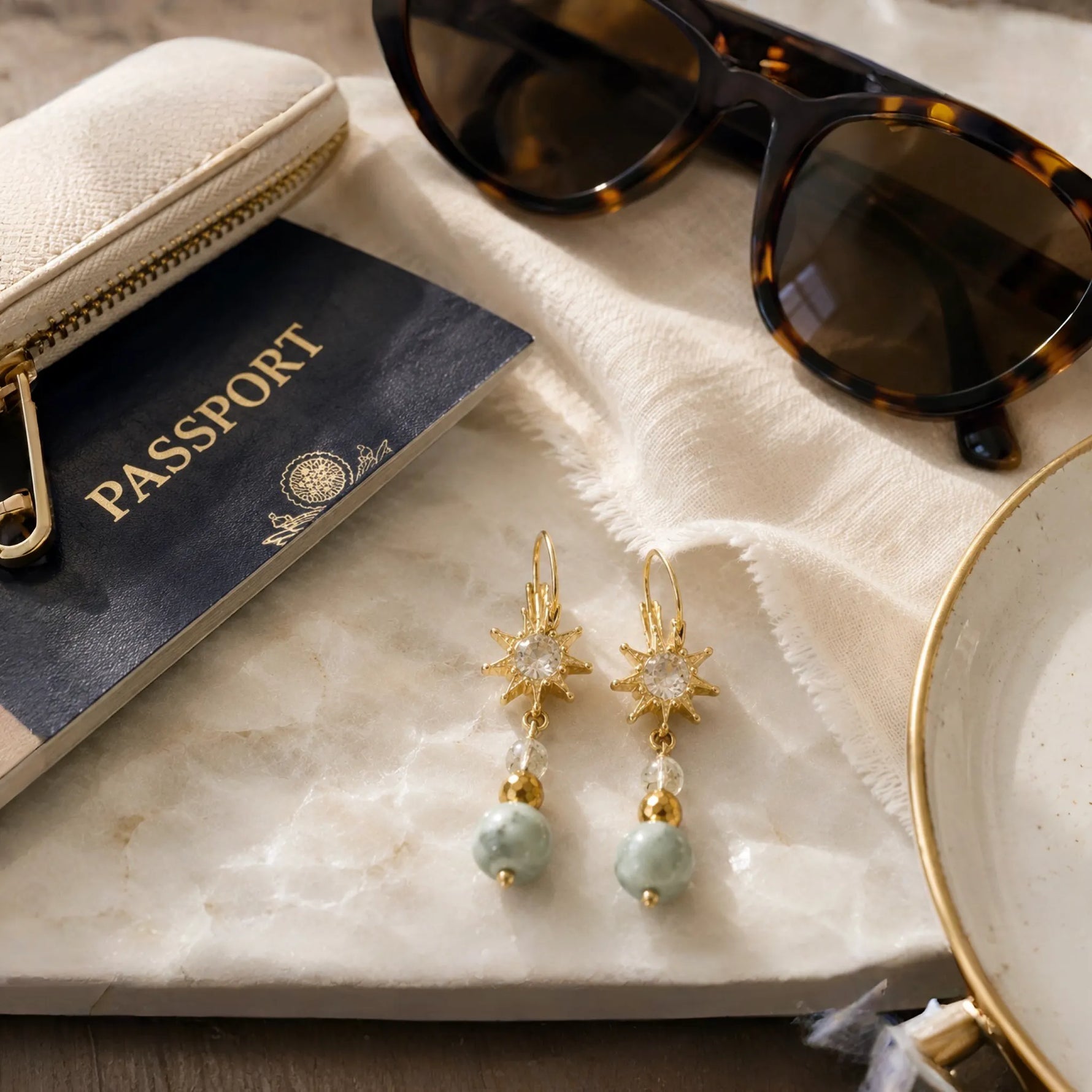 Quianna handcrafted lucky jade drop earrings styled with a passport, sunglasses, and luxury travel accessories on the Carabella signature white quartz background.