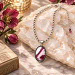 Sabine Tourmaline Pendant Necklace arranged on white quartz with burgundy flowers and warm candlelight, showing the silver-tone chain and three-stone tourmaline extender detail.