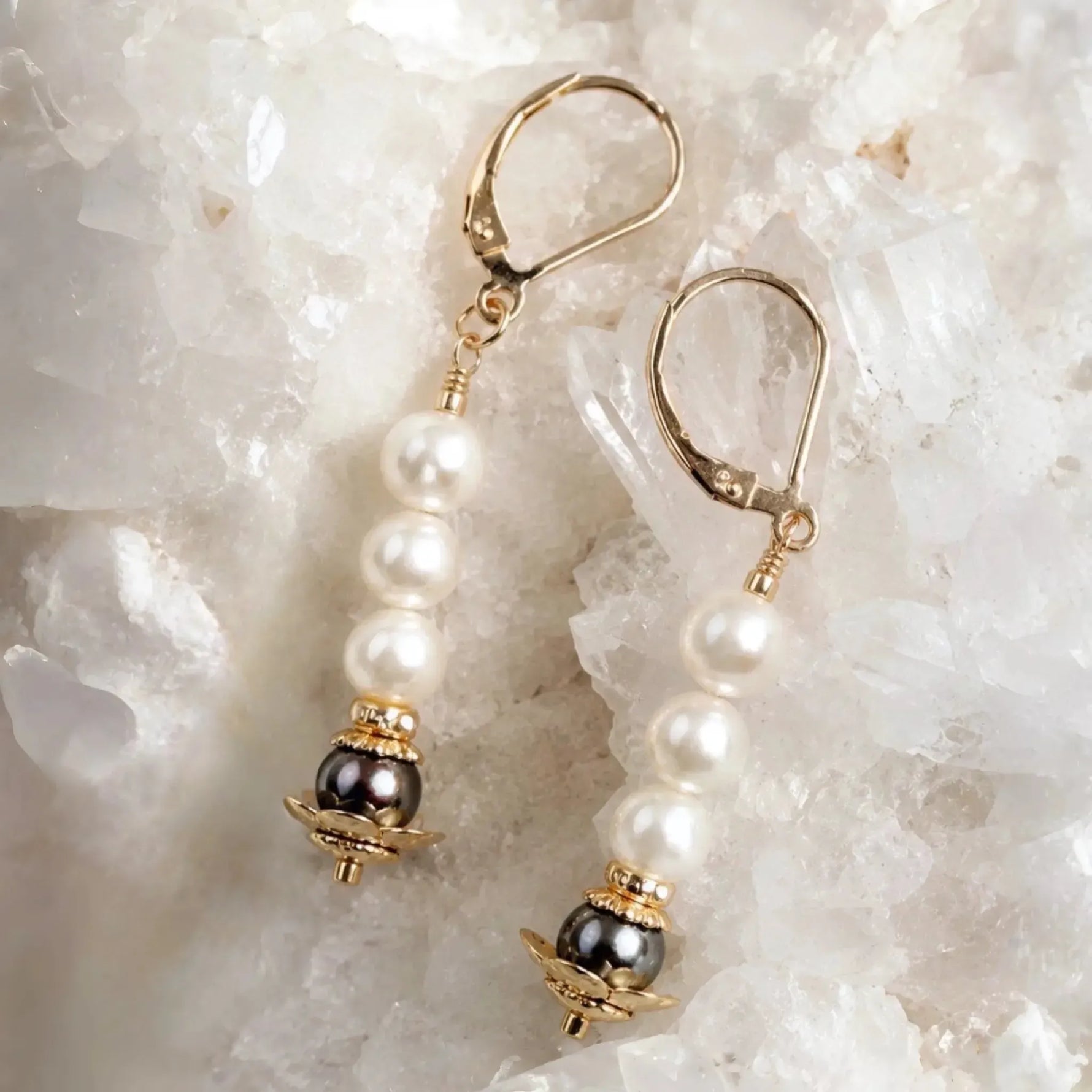 Serenity Swarovski® Crystal Pearl earrings with dark grey accent pearls and 14k gold-filled leverback ear wires displayed on a white quartz crystal cluster