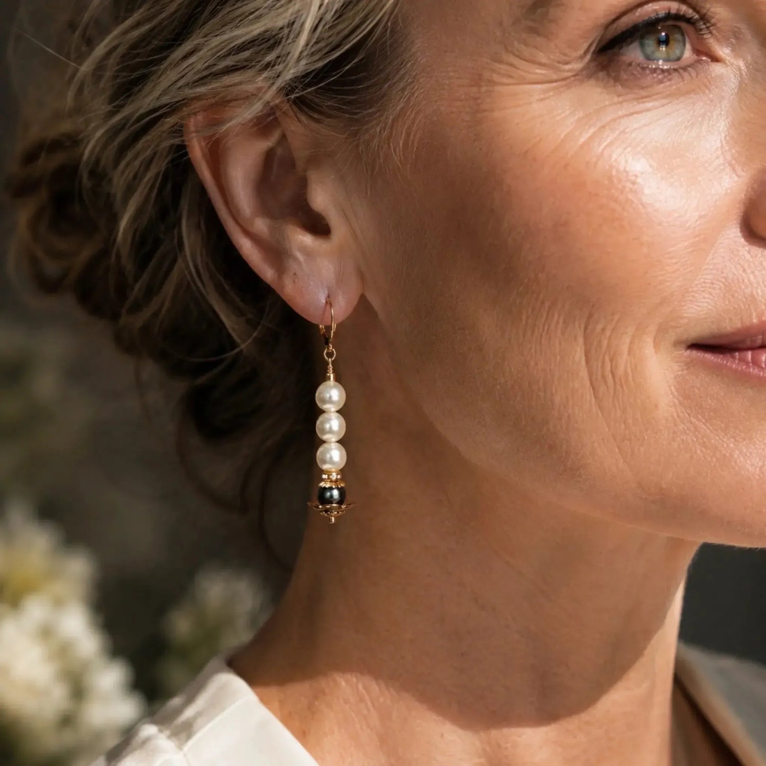 Serenity Swarovski® Crystal Pearl earrings worn by an elegant woman showcasing the 2-inch drop length, dark grey accent pearl, and 14k gold-filled leverback closure in warm natural light