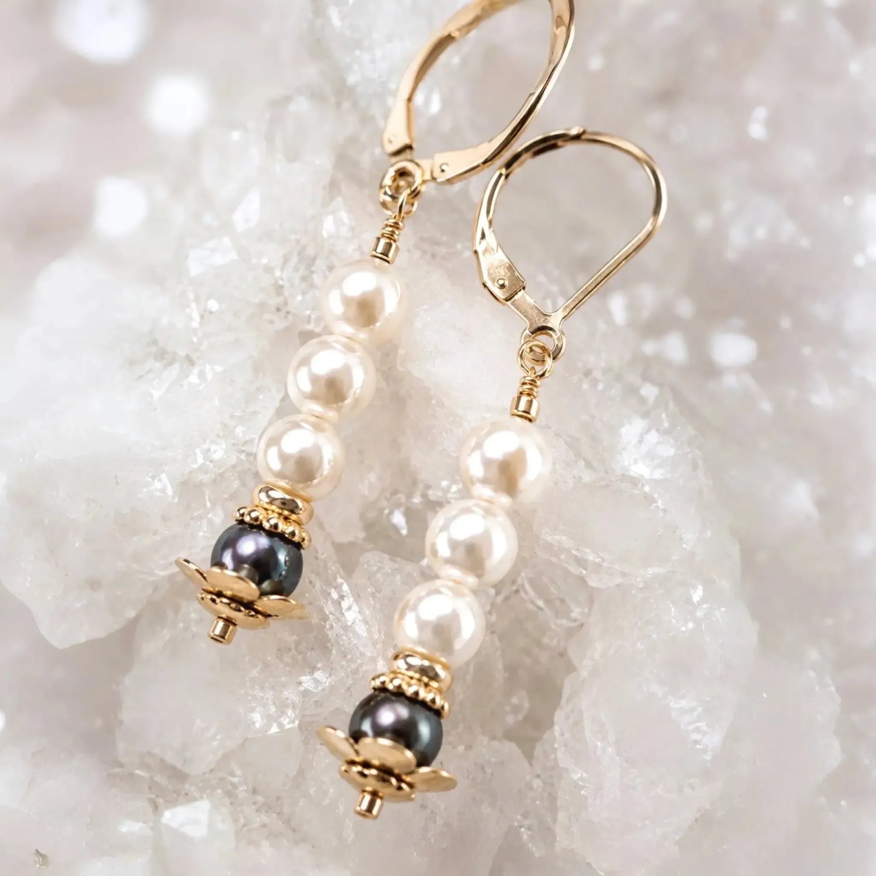 Serenity Swarovski® Crystal Pearl earrings with dark grey accent pearls and 14k gold-filled leverbacks displayed on a white quartz crystal cluster in a luxury macro close-up