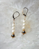 Serenity pearl drop earrings displayed on a light stone surface showing design details