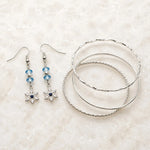 Snowflake crystal earrings paired with Lilith fine silver bangles arranged on white quartz, creating an elegant coordinated jewelry set handcrafted in Canada.