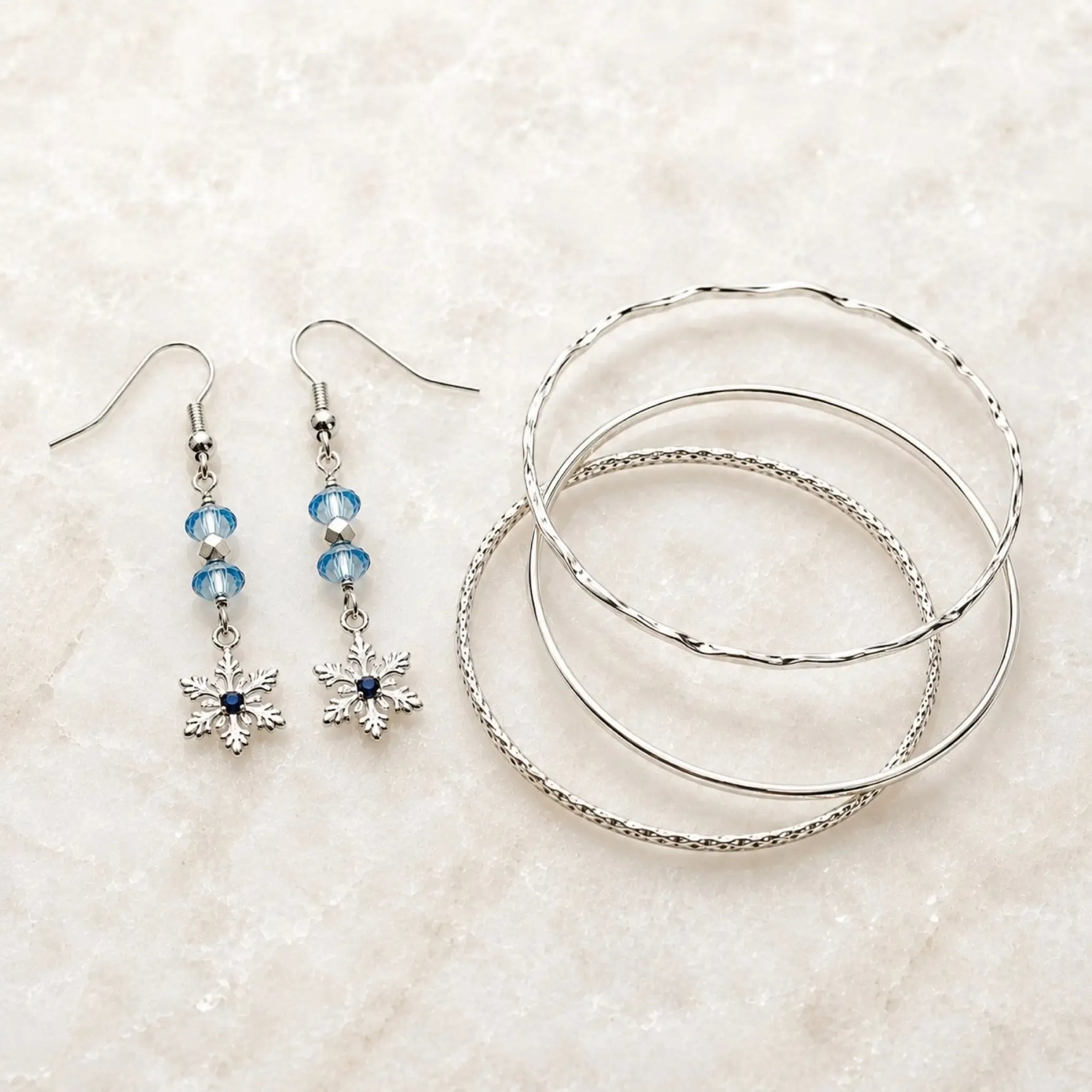 Snowflake crystal earrings paired with Lilith fine silver bangles arranged on white quartz, creating an elegant coordinated jewelry set handcrafted in Canada.