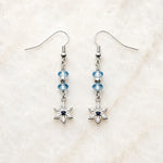 Handcrafted silver snowflake earrings with sapphire-blue crystals displayed on Carabella's signature white quartz surface.