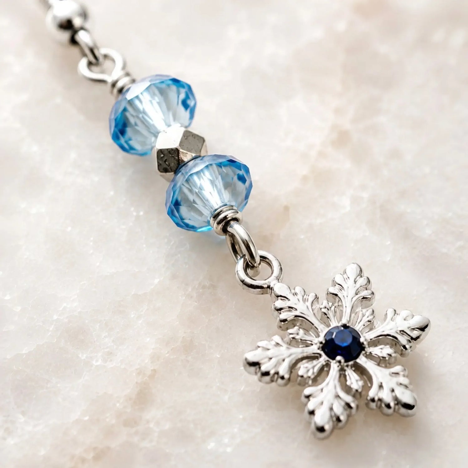 Close-up macro of handcrafted silver snowflake earrings highlighting faceted sapphire-blue crystals, polished metal details, and artisan craftsmanship.
