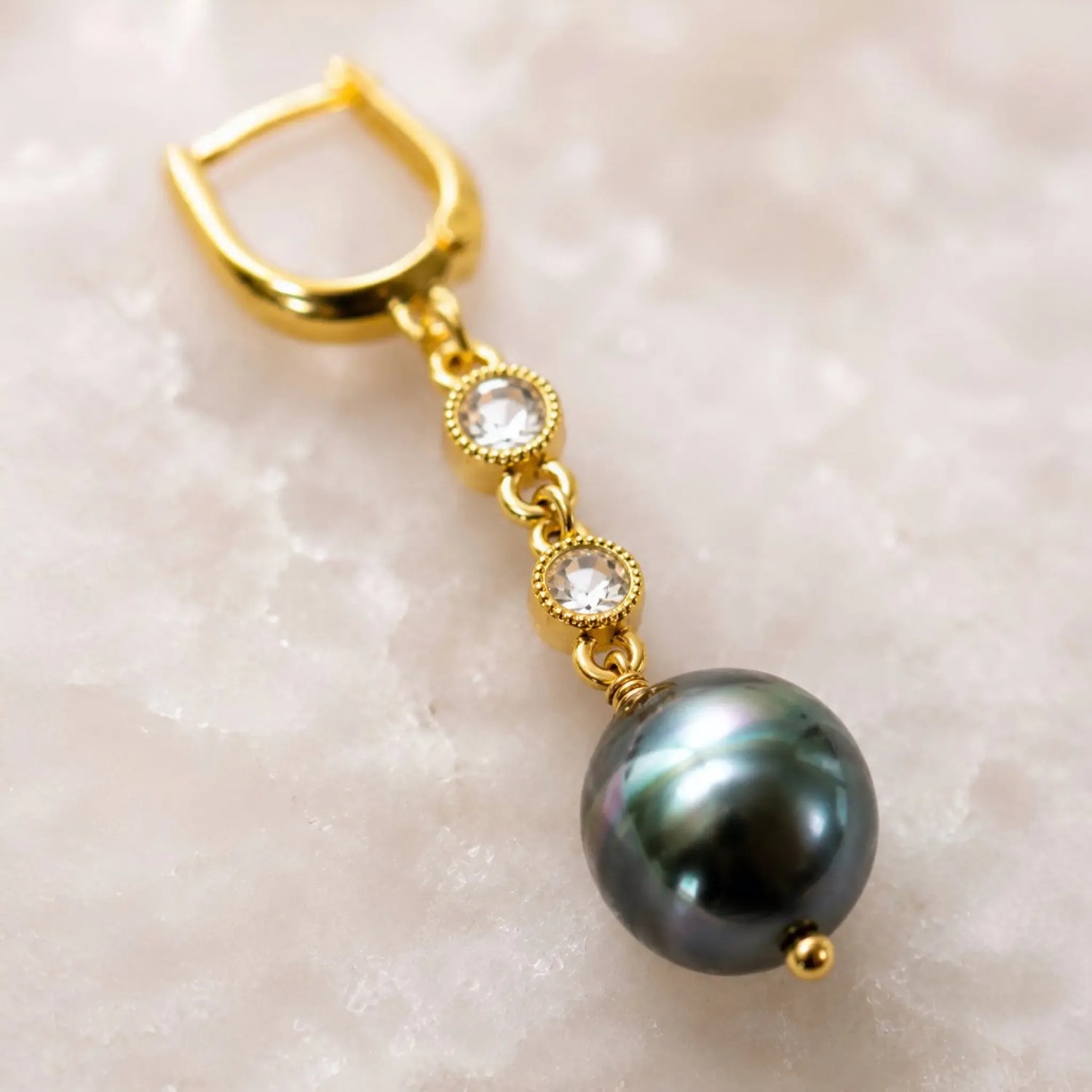 Luxury macro of a Tahitian South Sea black pearl earring highlighting natural pearl overtones, crystal bezels, gold wire wrapping, and handcrafted construction.