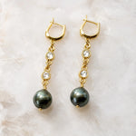 Tahitian South Sea black pearl drop earrings with crystal bezels and gold huggie hoops displayed on a white quartz background, handcrafted in Canada.