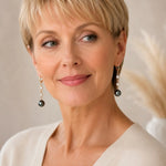 Three-quarter portrait of an elegant woman wearing Tahitian South Sea black pearl drop earrings with crystal accents and gold huggie hoops, showcasing both earrings.