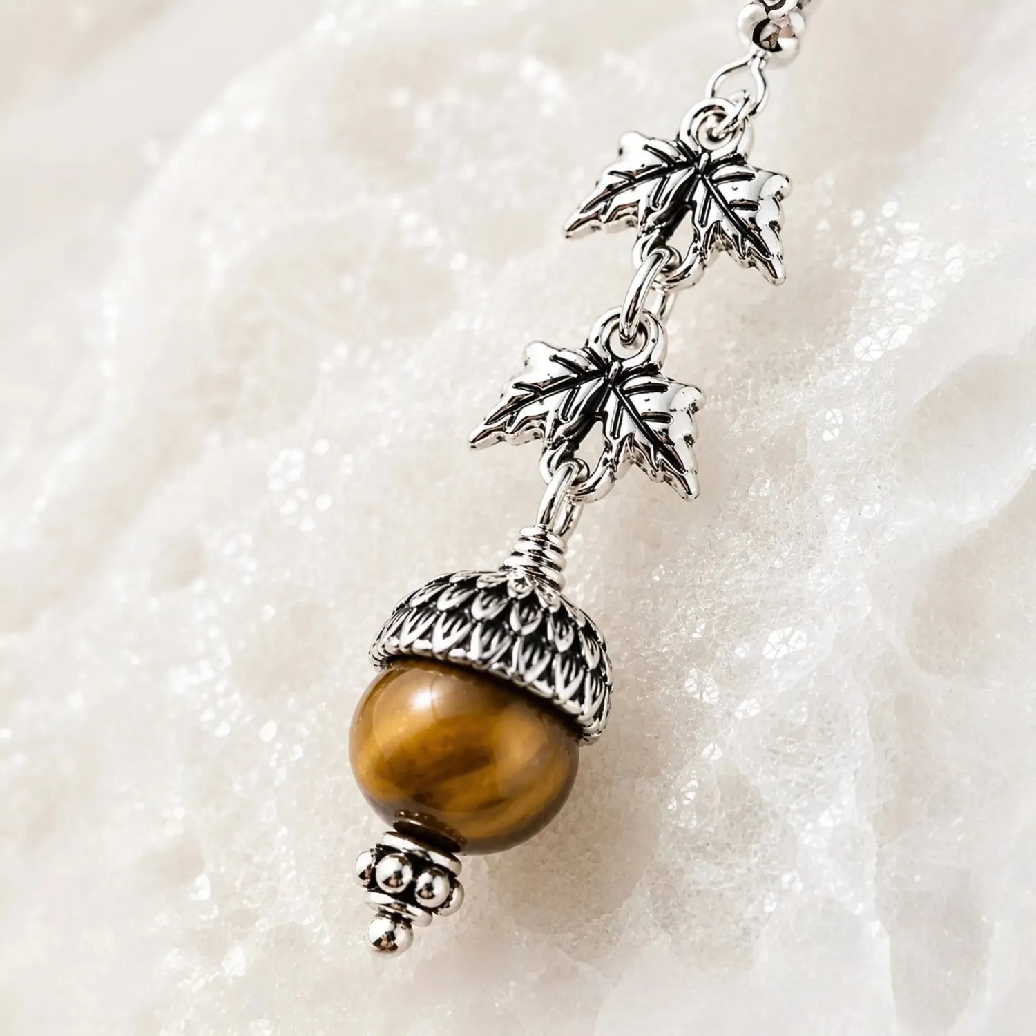 Close-up of handcrafted sterling silver maple leaf earrings featuring genuine Tiger's Eye gemstones and detailed acorn caps.