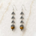 Handcrafted sterling silver Tiger's Eye maple leaf earrings displayed on Carabella's signature white quartz surface.