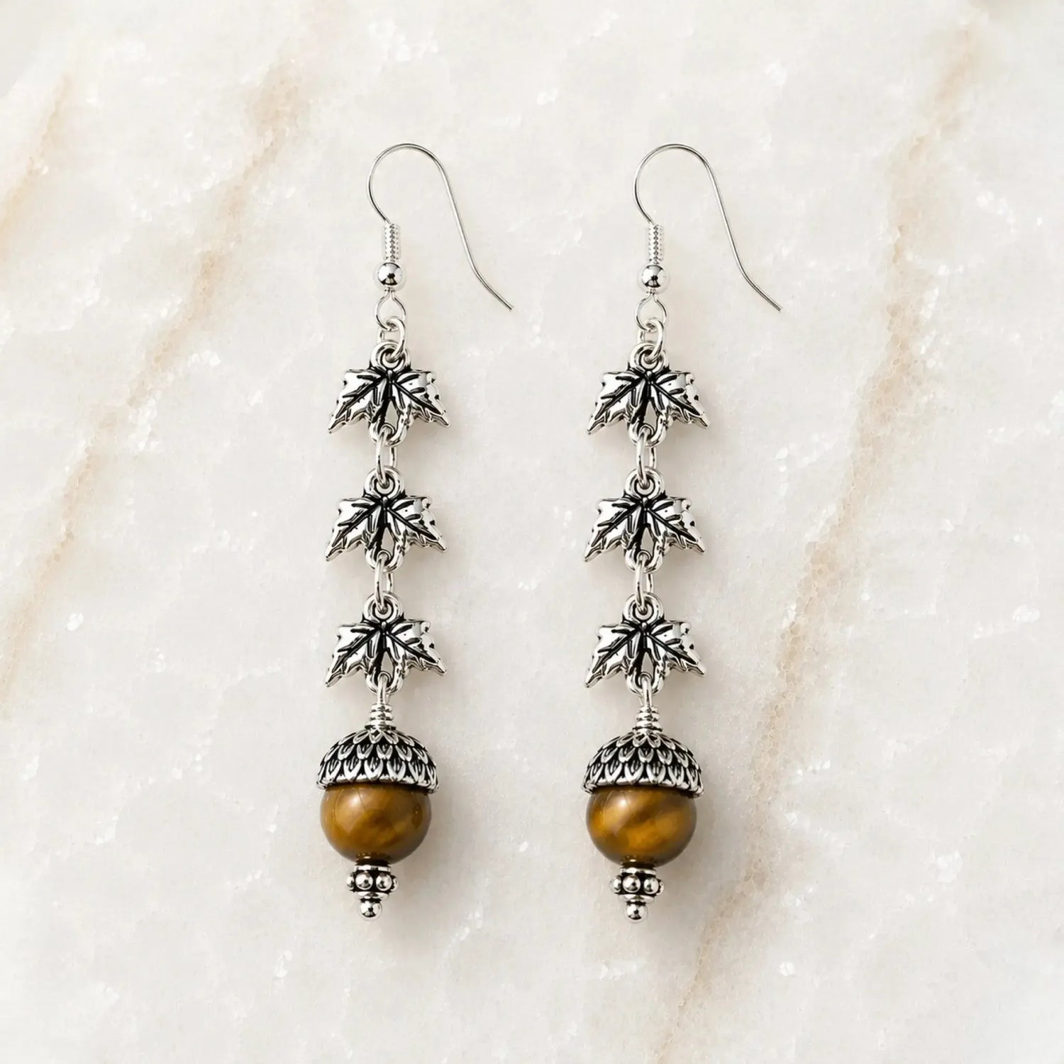 Handcrafted sterling silver Tiger's Eye maple leaf earrings displayed on Carabella's signature white quartz surface.