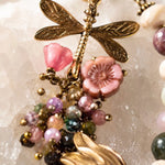 Close-up of Tulipe bracelet dragonfly charm with Czech glass flower and watermelon tourmaline gemstones on white quartz crystal.