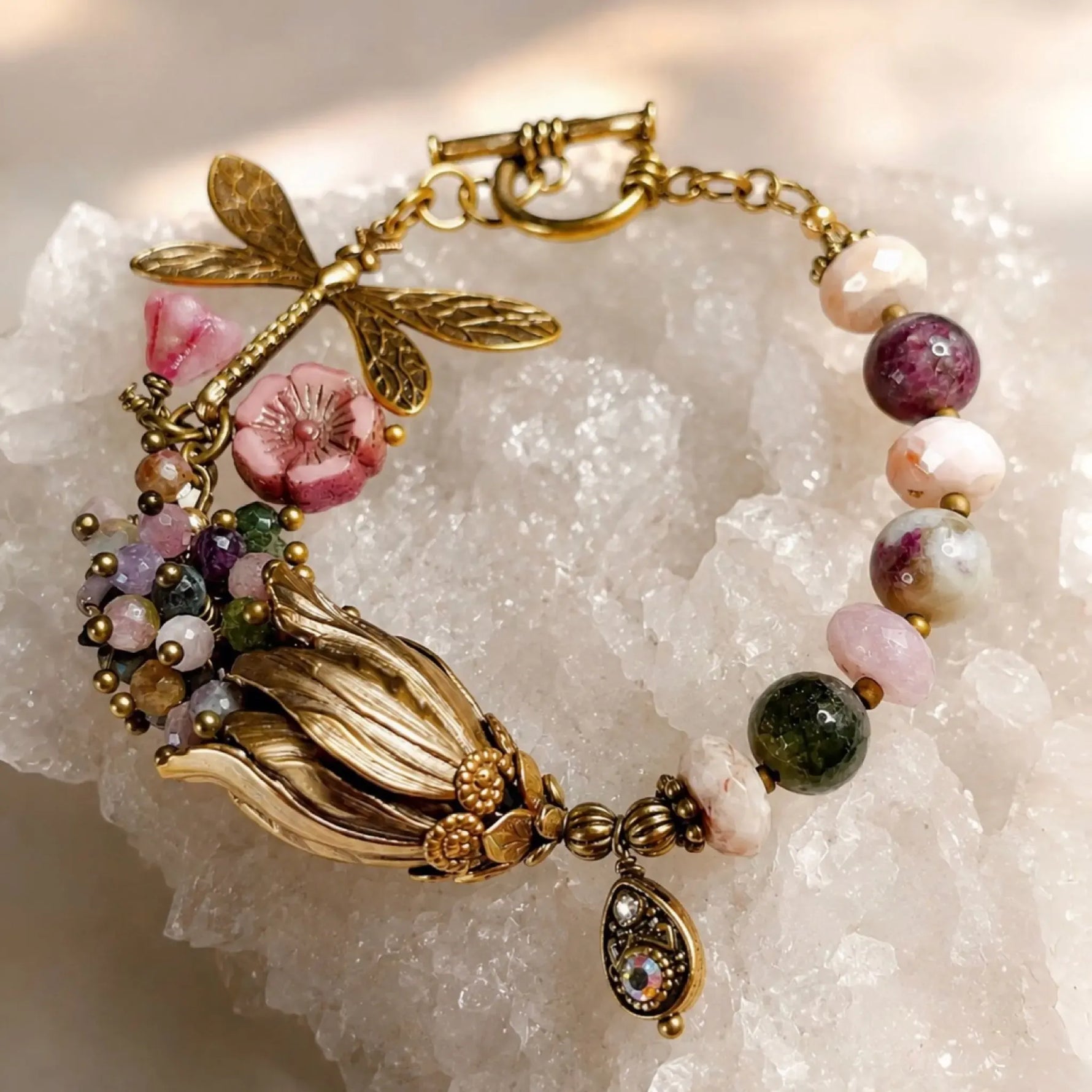 Tulipe bracelet with watermelon tourmaline gemstones, brass dragonfly charm, Czech glass florals, and tulip focal displayed on white quartz crystal.