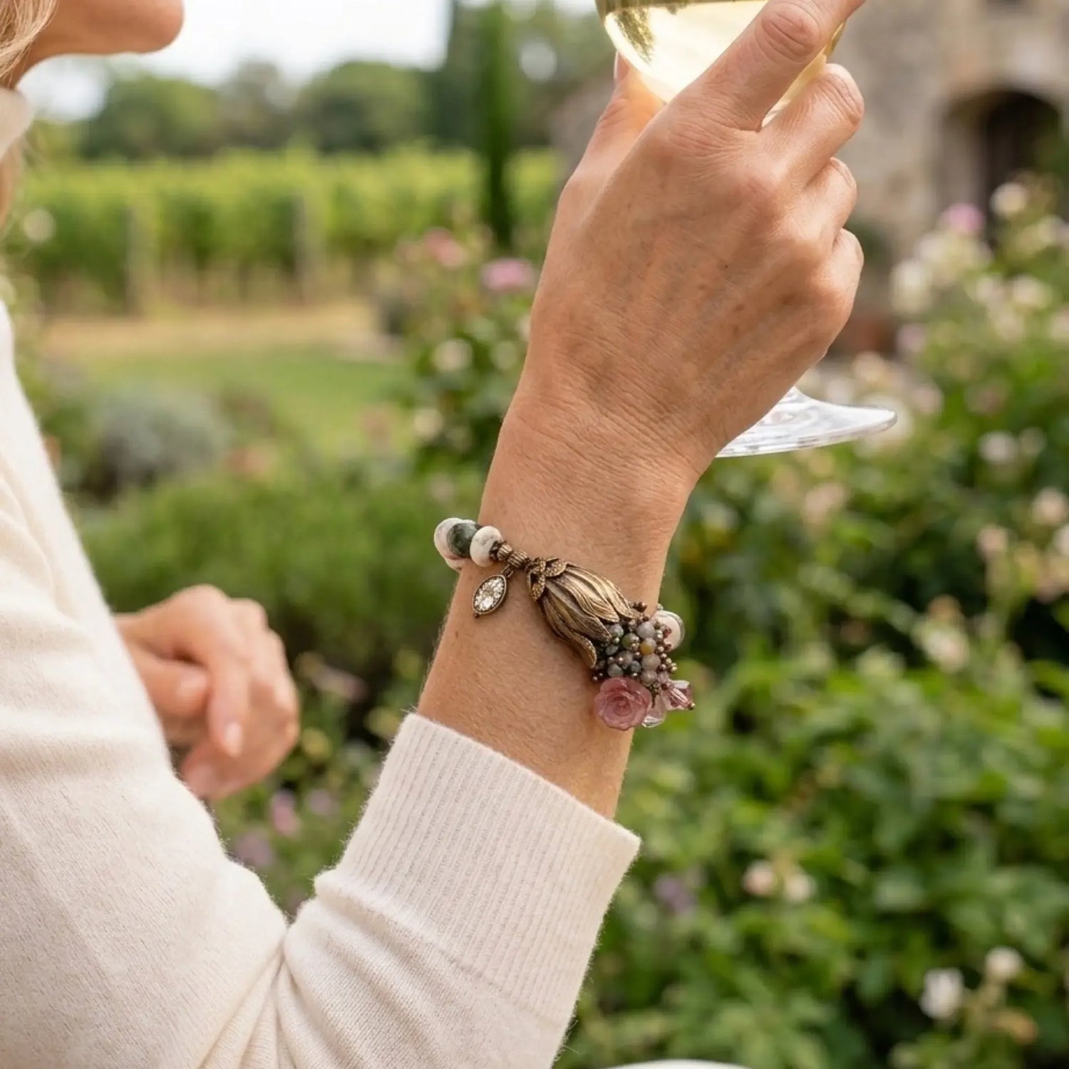 Woman wearing the Tulipe watermelon tourmaline bracelet at a winery garden, highlighting the brass tulip focal and gemstone details.