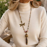 Elegant woman wearing the Tulipe watermelon tourmaline necklace over an ivory cashmere mock turtleneck in a refined garden lifestyle setting.