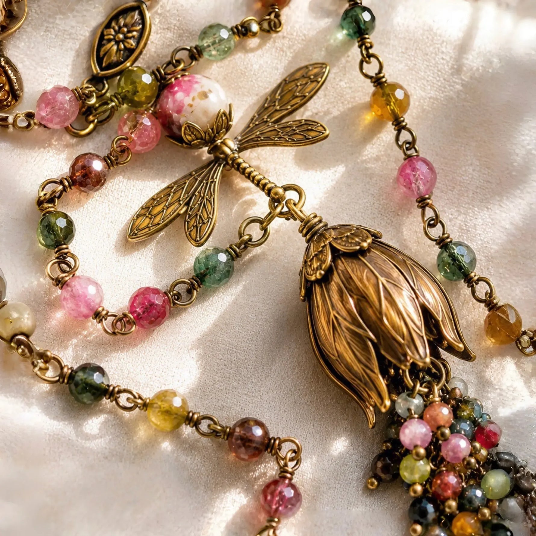 Macro detail of the Tulipe necklace highlighting faceted watermelon tourmaline gemstones, hand-wrapped wire construction, brass dragonfly charm, and tulip focal.