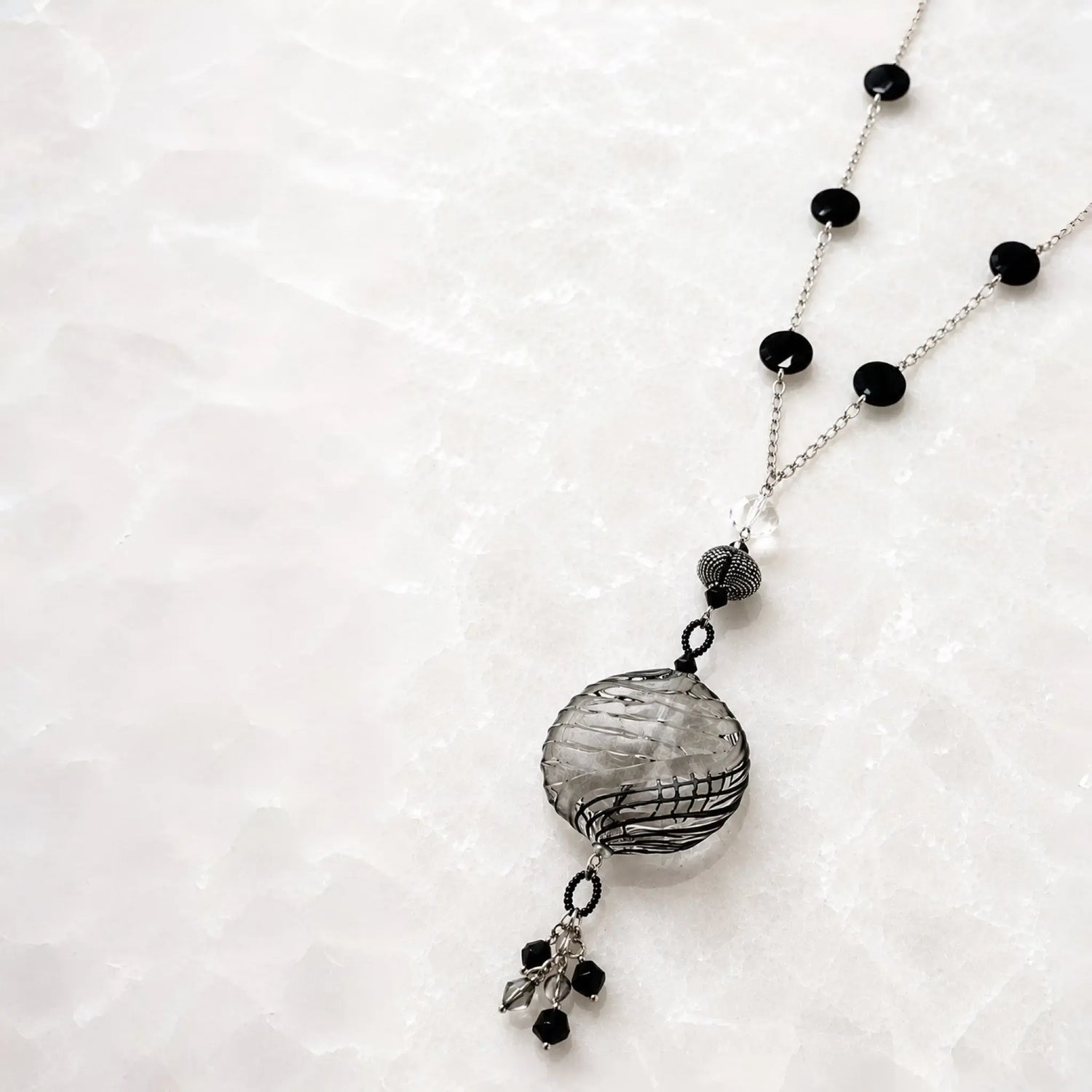 Angled view of the Venezia Murano glass necklace highlighting the dimensional hand-blown Murano glass pendant, sterling silver chain, artisan detailing and crystal tassel.