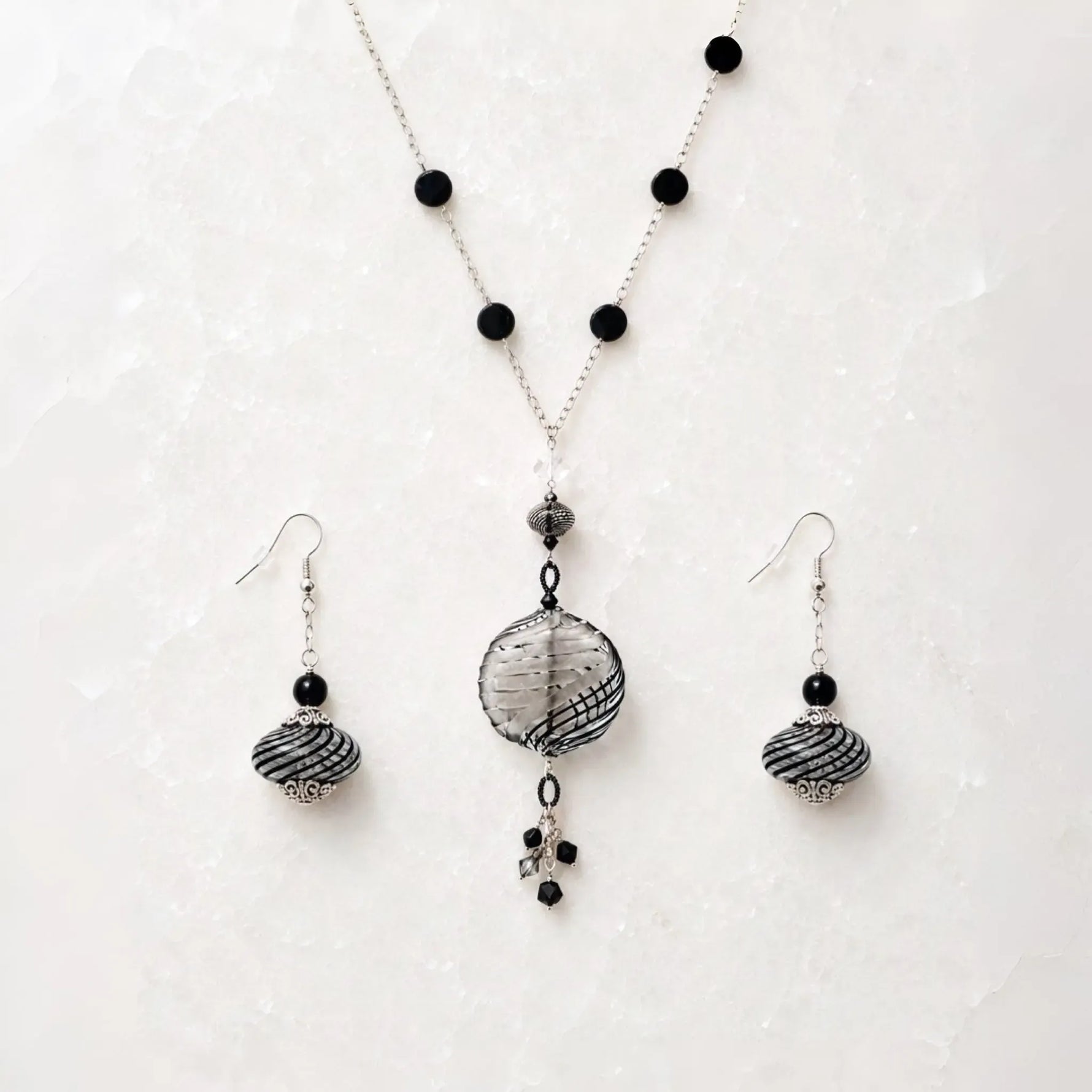 Venezia Murano glass necklace and matching drop earrings styled together on Carabella white quartz in a luxury flat lay.