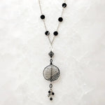 Venezia Murano glass necklace handcrafted in Canada with sterling silver chain, black Murano glass stations, artisan Murano pendant and crystal tassel on white quartz background.