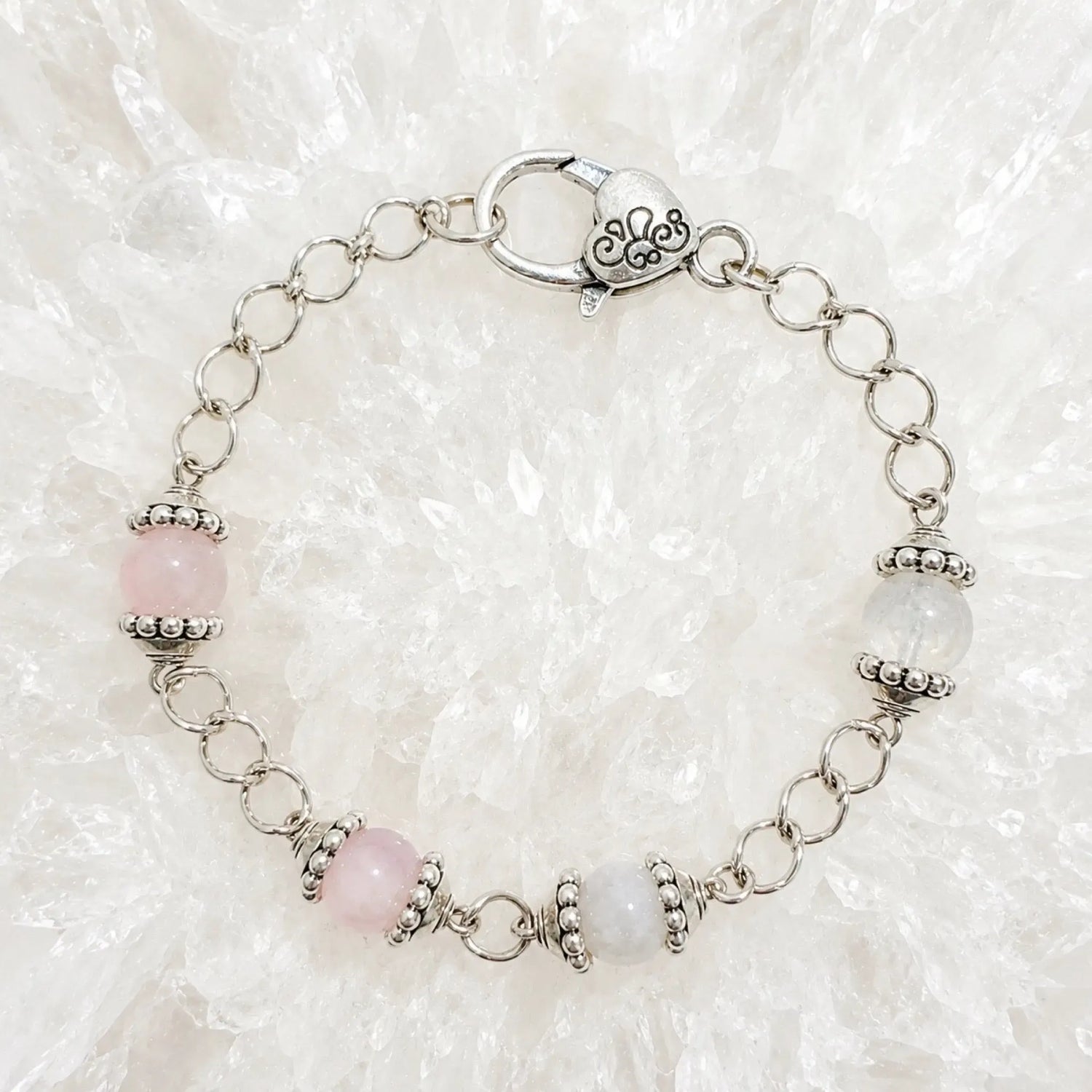 Venus Bracelet featuring rose quartz and moonstone gemstones with sterling silver accents arranged on luminous white quartz crystal.